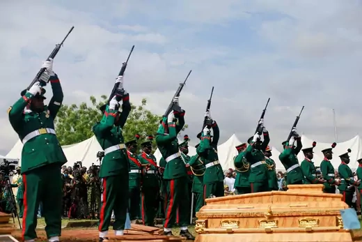 A line of Nigerian military officers raise their guns in salute at a funeral for a military general and others killed in a plane crash.
