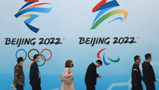 People wear protective masks as they walk in front of logos for the 2022 Beijing Winter Olympics.