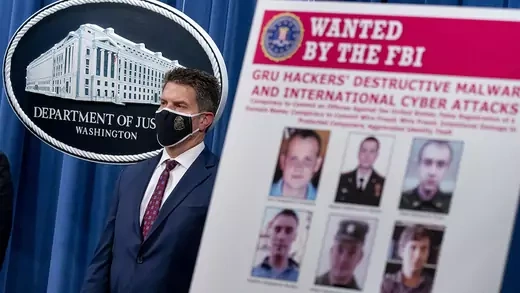 A poster showing six wanted Russian military intelligence officers is displayed with FBI Deputy Director David Bowdich in the background