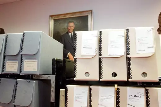 A stack of boxes containing volumes of the Pentagon Papers sit in front of a portrait of Lyndon B. Johnson. 