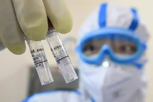 A technician wearing goggles and other protective gear holds up virus samples at a laboratory in Hengyang, China, in February 2020.