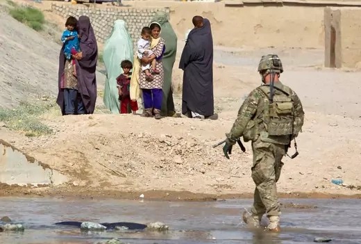 A soldier walks toward several Afghan women and children