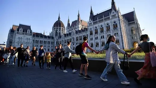 Protestors march around the Hungarian parliament holding hands