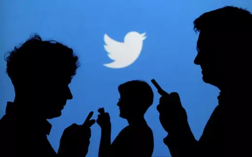 People holding mobile phones are silhouetted against a backdrop projected with the Twitter logo in this illustration picture taken September 27, 2013.