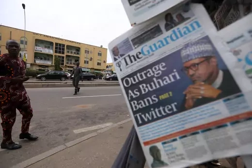 A picture of the cover of the Nigerian newspaper The Guardian with the headline "Outrage As Buhari Bans Twitter" and a picture of Nigerian President Muhammadu Buhari. A man looks at the newsstand selling the paper.
