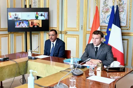 French President Emmanuel Macron and Nigerien President Mohamed Bazoum sit at a table with their countries' flags behind them, along with an EU flag. Other leaders of G5 Sahel countries are seen on a screen in the background.