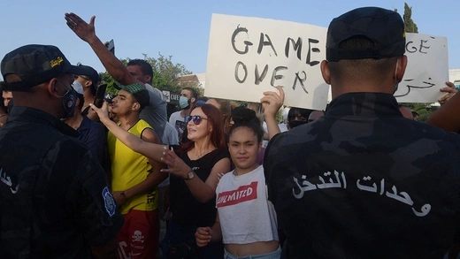 Amid fellow protesters, a Tunisian girl holds a sign reading "game over." Two soldiers stand facing the crowd.