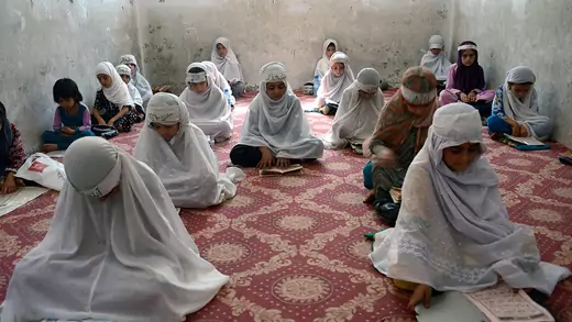 Girls sit on the floor and read from books in a classroom. 