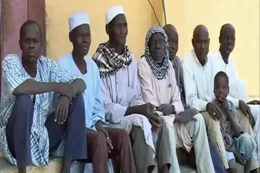 Eight people, all male, with ages ranging from childhood to older adulthood, sit looking towards a camera.