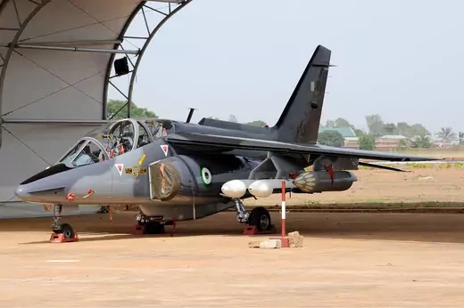 An Alpha Jet sits idle at an airport with missiles and munitions held under the wings.