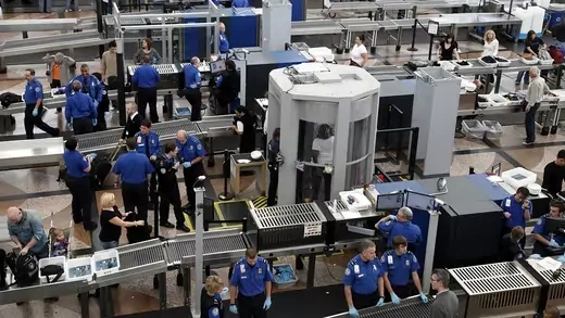 TSA workers conduct security checks, including full-body scans, at a crowded Denver International Airport.