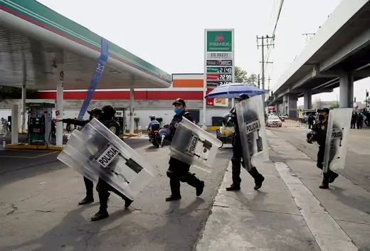 Police officers holding shields cross in front of a gas station in Mexico City