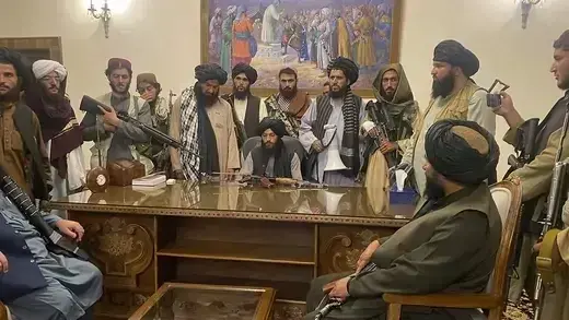 Taliban fighters stand behind a desk in the Afghan presidential palace.