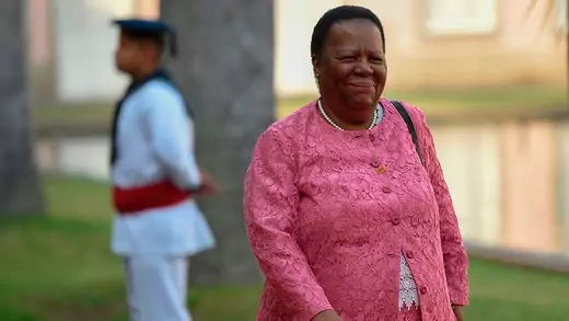 Minister Naledi Pandor walking with a man in uniform in the background.