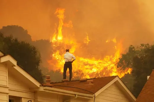 A man on a rooftop looks at approaching flames as the Springs fire continues to grow on May 3, 2013 near Camarillo, California. The wildfire has spread to more than 18,000 acres on day two and is 20 percent contained.