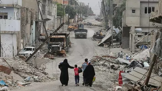 A displaced Iraqi family walks along a Mosul street of rubble and broken building