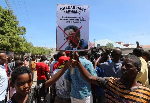 Protesters hold up a sign with a red "X" drawn across a picture of the Somali president.