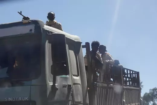 Several individuals stand in back of an armed truck.