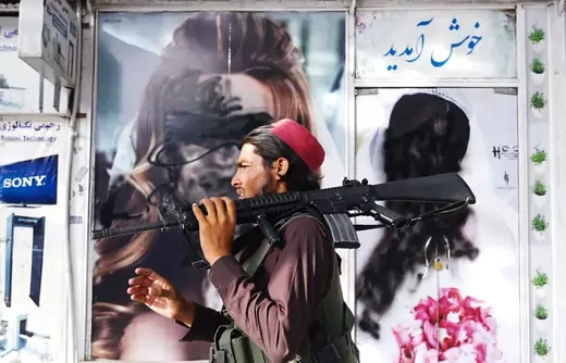 A Taliban fighter holds a gun and walks past a beauty salon with images of women painted over.