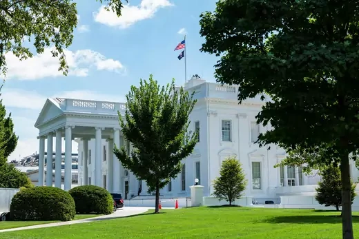 White House exterior is seen through trees on a sunny day.