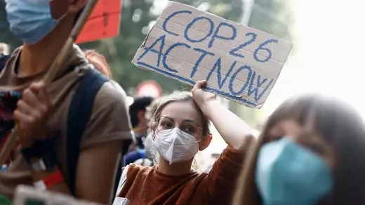 A person holds a sign reading "COP26 act now."