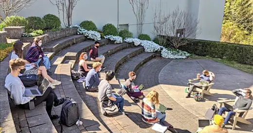 Students with laptops and backpacks sit in an amphitheater, facing two instructors who sit in Adirondack chairs.