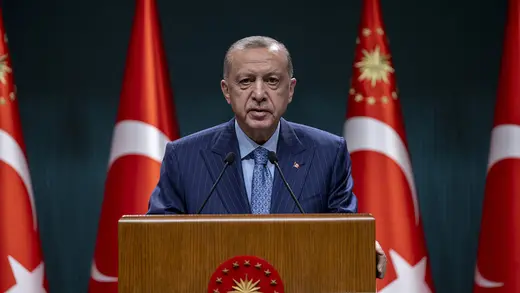 Turkish President Recep Tayyip Erdogan speaks at a lectern. There are four Turkish flags hanging behind him.