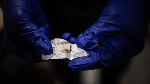 A close-up of a police officer wearing gloves holding a small amount of heroin and fentanyl wrapped in a piece of paper.