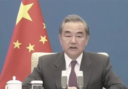 Wang Yi, wearing a dark suit and purple tie, speaks into a microphone, with the Chinese flag in the background.
