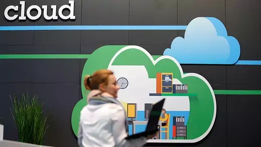 A woman holding a laptop in front of a cloud computing logo at the booth of IBM
