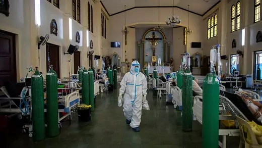 Health care workers in protective gear walking through a row of beds