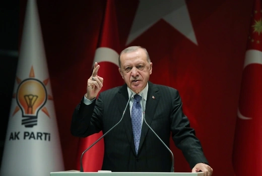 Turkish President Recep Tayyip Erdogan speaks at a lectern. There are Turkish and AKP flags behind him.
