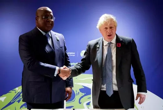 British Prime Minister Boris Johnson and DRC President Felix Tshisekedi, both wearing suits, shake hands in front of a stylized globe.