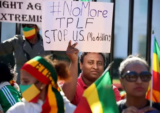A protester holds a sign reading "#NoMore TPLF STOP U.S. Meddling" amid a group of protesters holding Ethiopian flags.