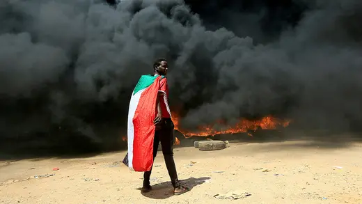 A person wearing a Sudanese flag stands in front of black plumes of smoke during a protest in Khartoum on October 21, 2021.