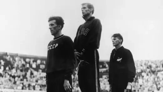 Three men stand on risers during an Olympic medal awards ceremony.