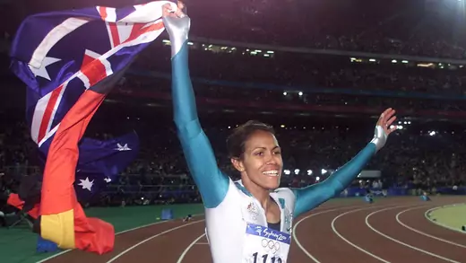 Cathy Freeman smiles and waves both the Aboriginal and the Australian flags on the track.
