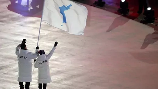 Two people wave a flag showing the Korean Peninsula. 