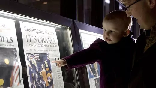 An 18 month old baby girl is carried by her father as they view the front page newspaper in the Newseum in Washington, D.C. after the historic presidential win by Democrat Barack Obama in 2008