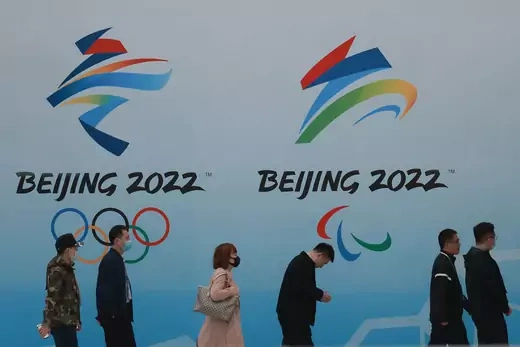 People wear protective masks as they walk in front the logos of the 2022 Beijing Winter Olympics at National Aquatics Centre on April 9, 2021 in Beijing, China.