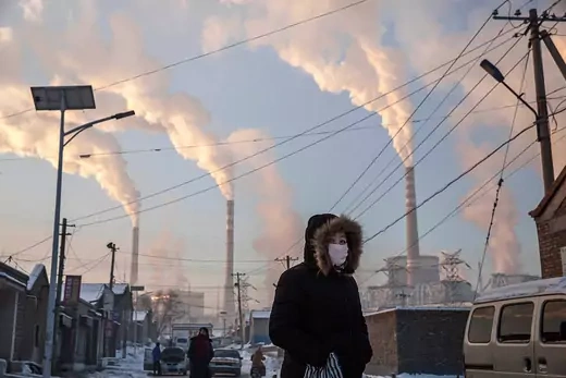 Smoke billows from stacks as a Chinese woman wears as mask while walking in a neighborhood next to a coal fired power plant on November 26, 2015 in Shanxi, China.