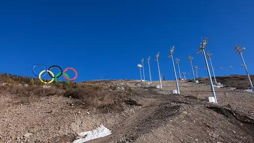 The Olympic rings appear on a ski hill that lacks snow.