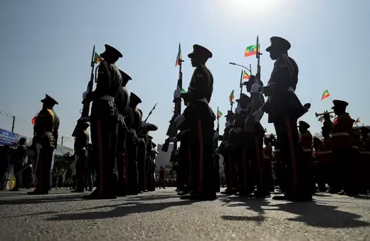 Ethiopian armed forces march carrying weapons and small Ethiopian flags during a pro-government rally.