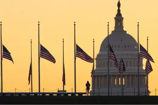 American flags surrounding the Washington Monument fly at half-staff as the sun sets behind the U.S. Capitol Building. 