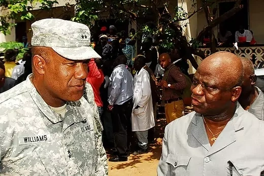 U.S military commander wearing camouflage speaks with former Liberian minister in civilian clothing. 
