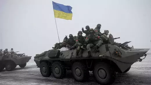 Ukrainian soldiers sit atop an military carrier with a Ukrainian flag.