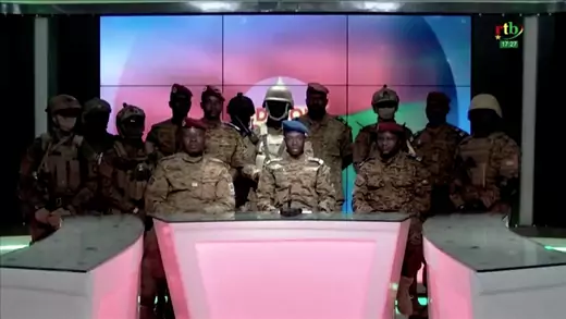 A group of military personnel wearing camouflage give an announcement on broadcast television.