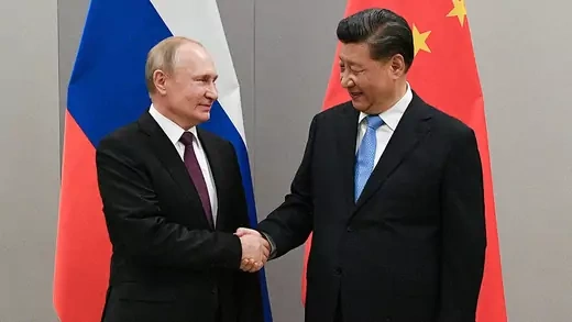 Russian President Vladimir Putin shakes hands with Chinese President Xi Jinping with their flags in the background.