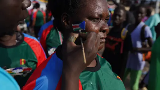An artist is painting a South Sudan flag on a woman's cheek, after The Great South Sudan Run, at John Garang Mausoleum, during the country's 10th anniversary since independence, on July 9, 2021 in Juba, South Sudan. 