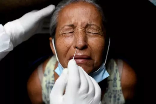 A health-care worker takes a swab sample to test for COVID-19 from a woman who looks up with her eyes closed and her mask pulled down below her chin.